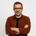 Andrés Salvat, autor de El Espectro, posando con chaqueta color teja y gafas negras sobre fondo blanco, con gesto irónico y seguro